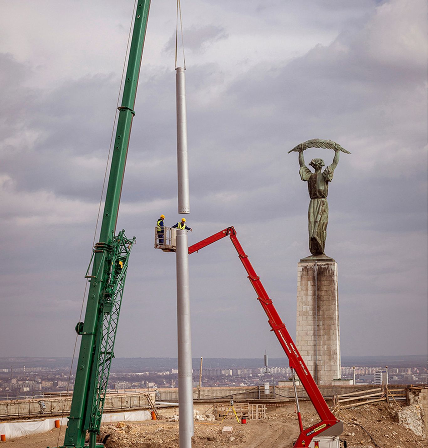 A nemzeti lobogó árbócának felállítása daruval a Citadella udvarán, háttérben a Szabadság-szobor